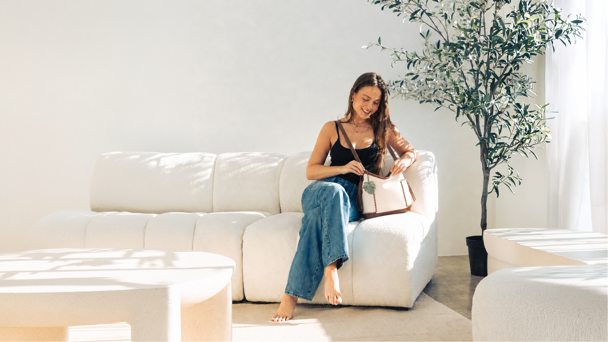 Woman sitting on a white couch in a modern living room with a plant in the background.